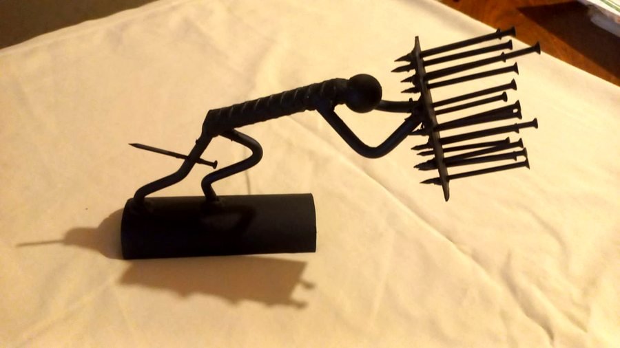 Escultura metálica de figura humana empujando contra pared de clavos — obra artística en metal negro con acabado mate, HeraldWeid